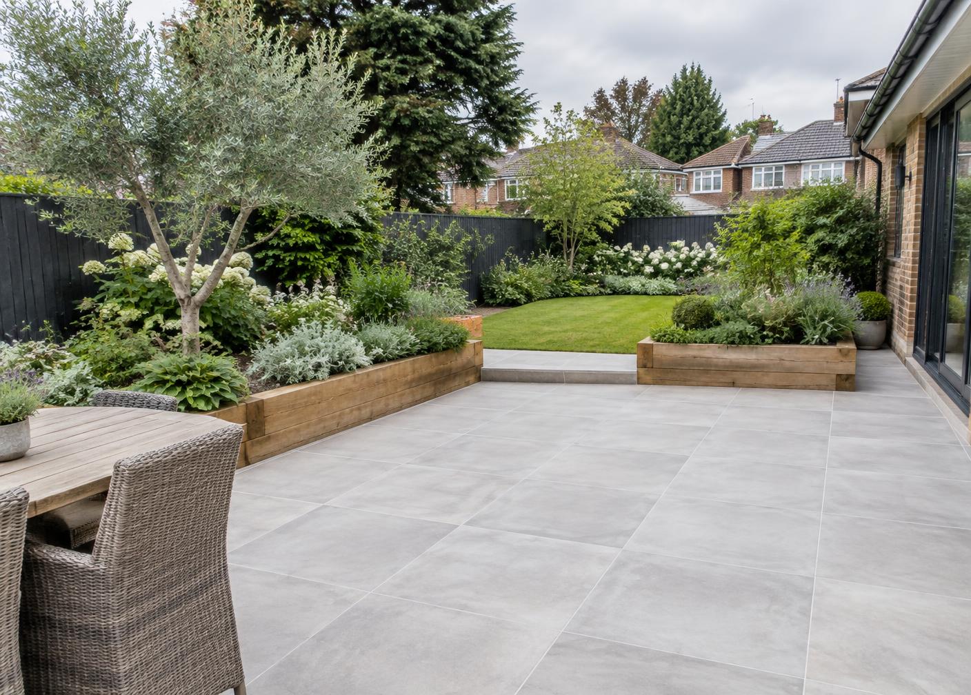 Large-format grey porcelain patio with sleeper-edged planting beds, layered greenery and a lawn